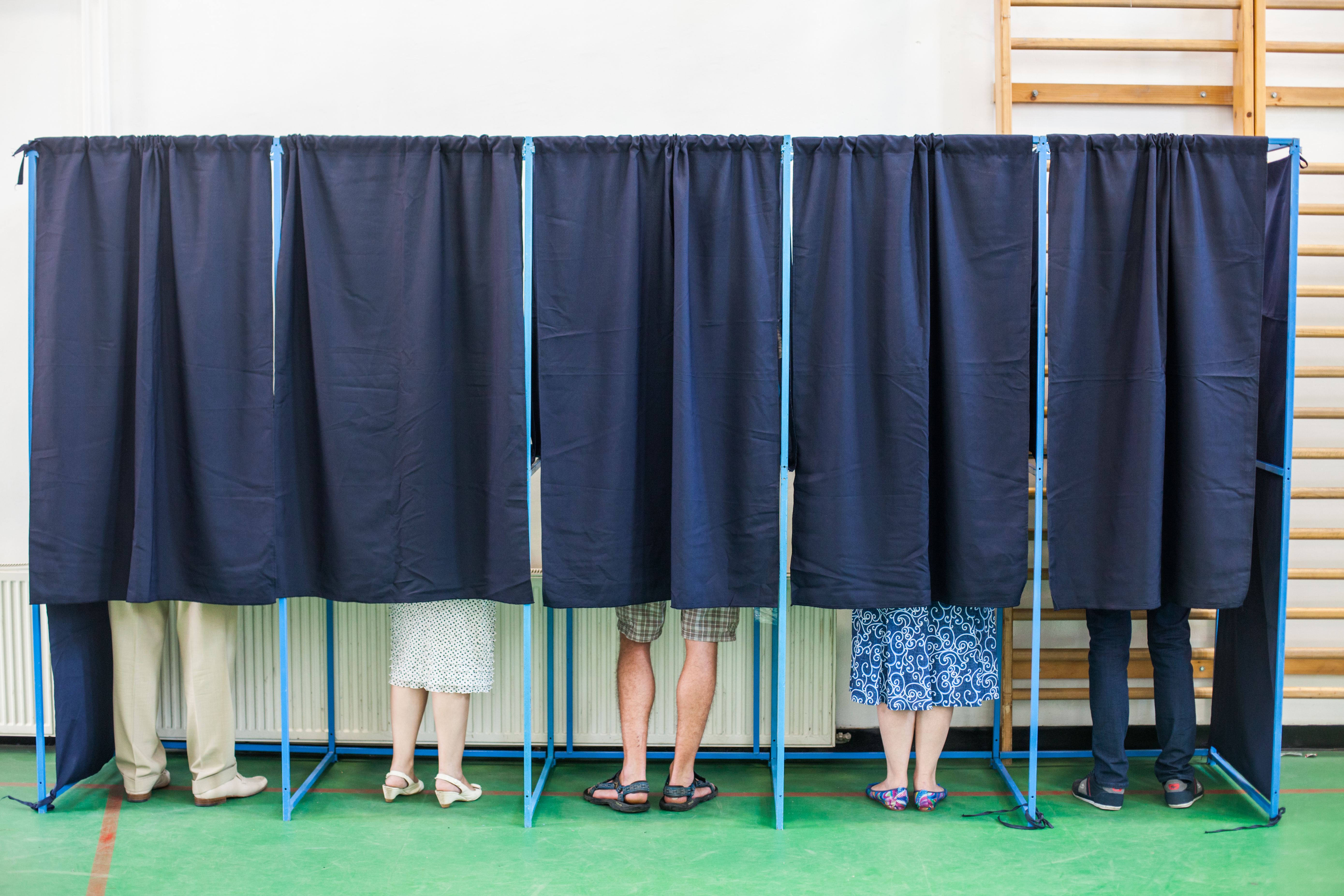 People standing behind curtains at a polling/voting station