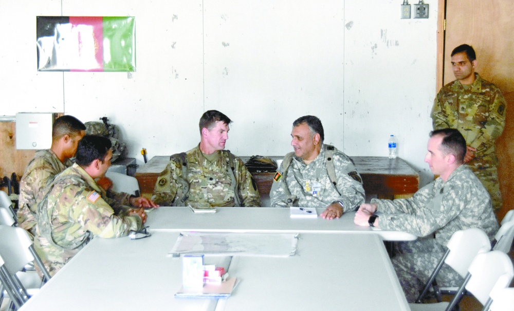 A group of men in military uniforms seated around a table, talking, interpreter in background