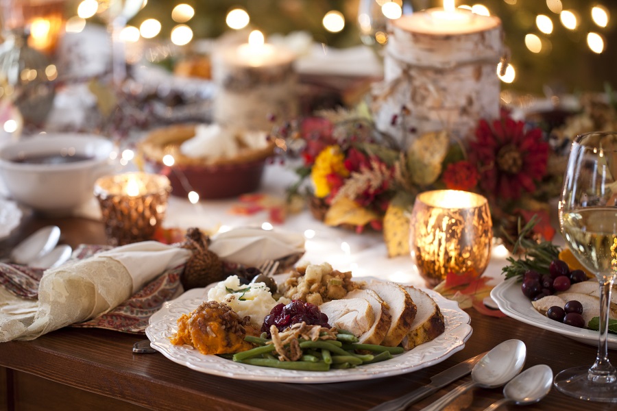 Close-up shot of a dish on a festively-decorated table. The plate has traditional Thanksgiving dishes on it: turkey, green beans, cranberry sauce, sweet potatoes, mashed potatoes, and stuffing.