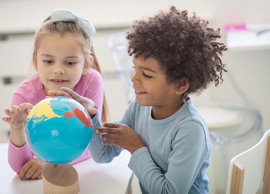 Two children sitting at a table, looking at a small globe.