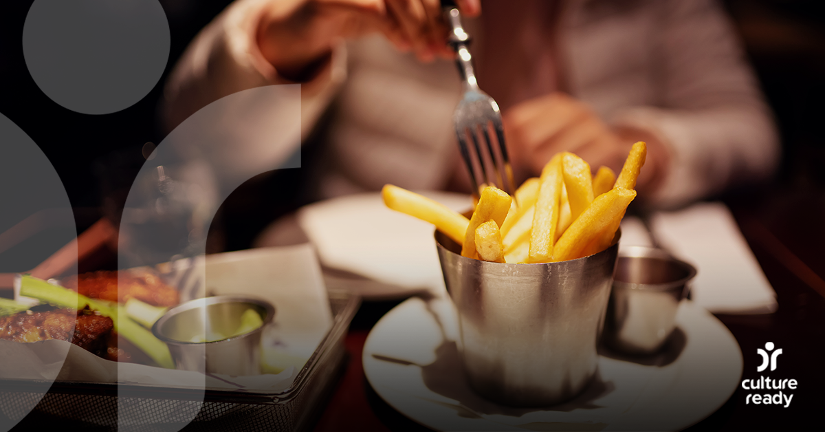 Close-up image of a cup of french fries. The person who is eating them is using a fork.