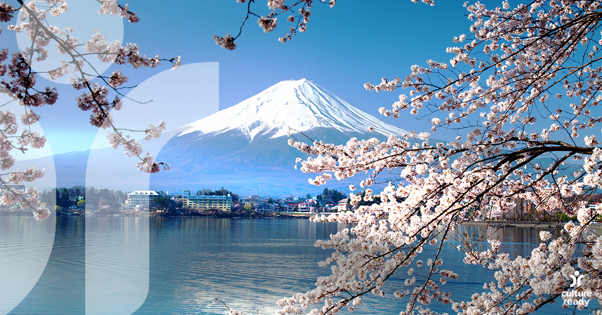 A pink Cherry Blossom tree in the foreground with a blue lake and Mt. Fuji in the background