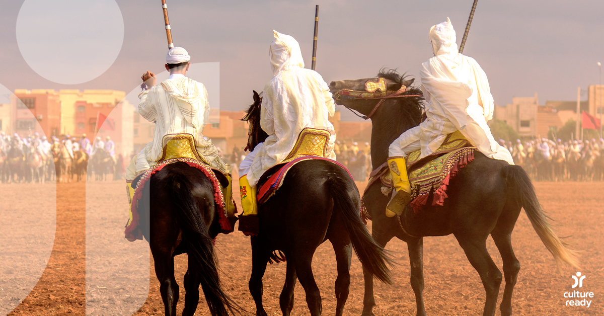 Three men dressed in white ride elaborately decorated horses participate in Tbourida