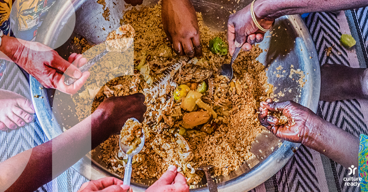 Seven hands are reaching into a communal dish of rice and fish