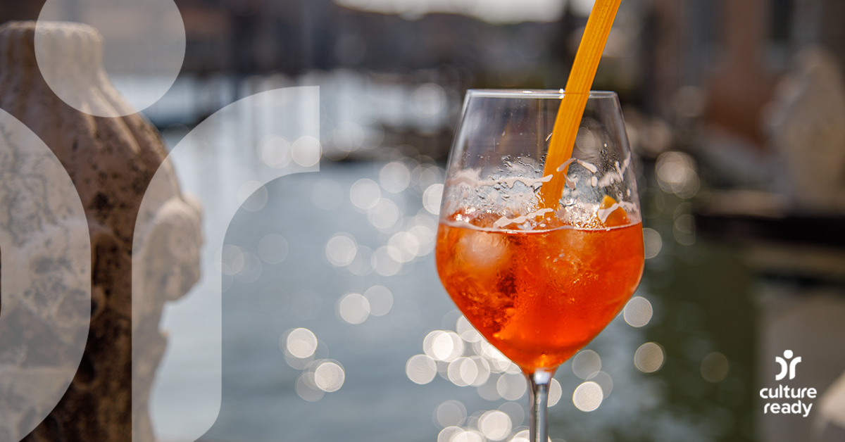 A wine glass with red wine sits in front of a sparkling river, there is a pasta straw in the glass