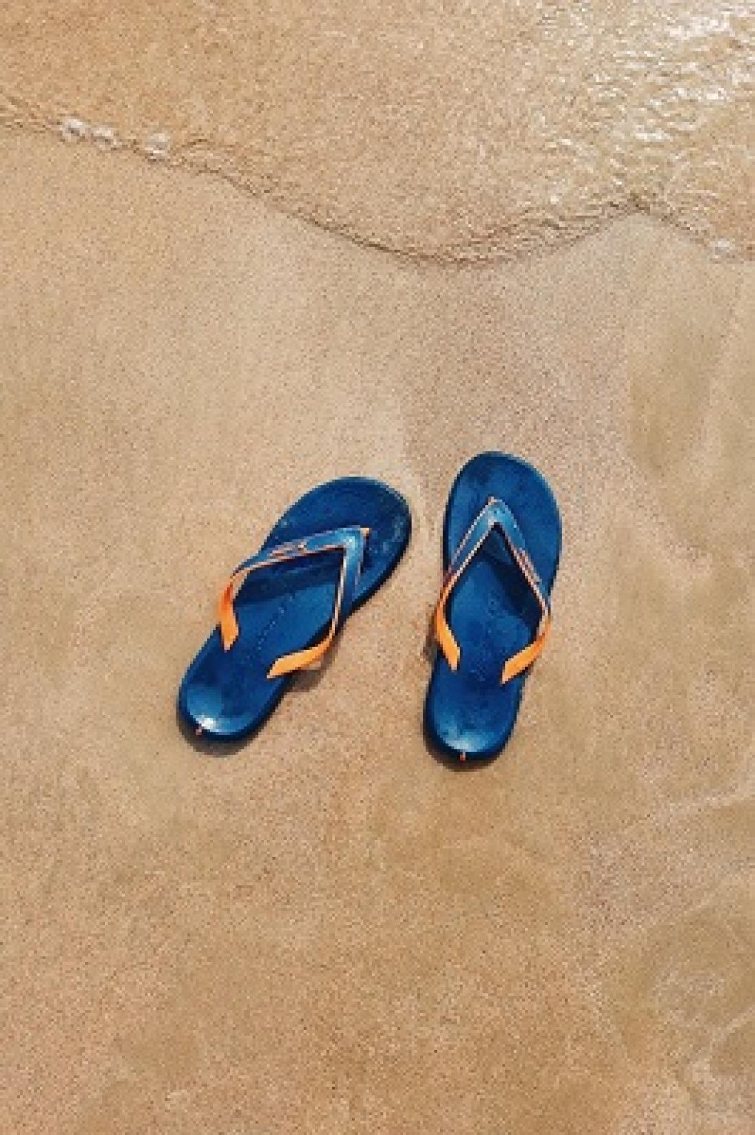Blue flip flops on the sand with water approaching