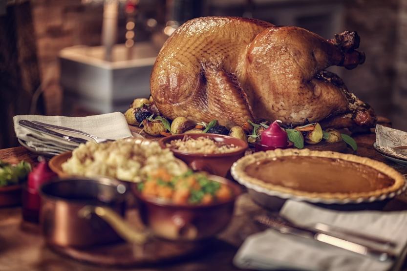 A cooked turkey sits on a table next to a pumpkin pie and other side dishes.