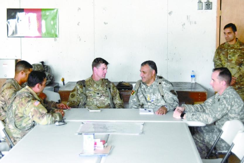 A group of men in military uniforms seated around a table, talking, interpreter in background