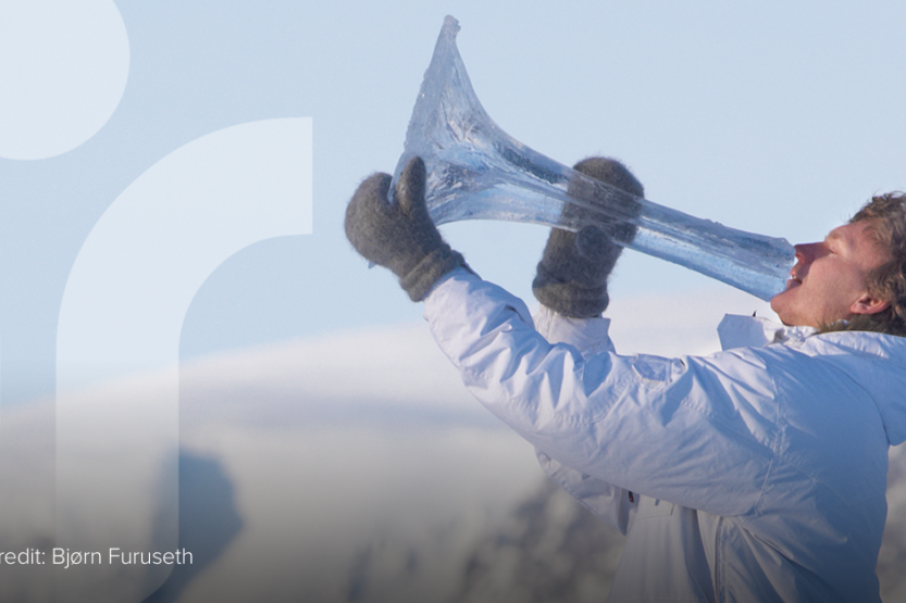 A man in a white coat and black gloves plays a horn instrument made out of ice