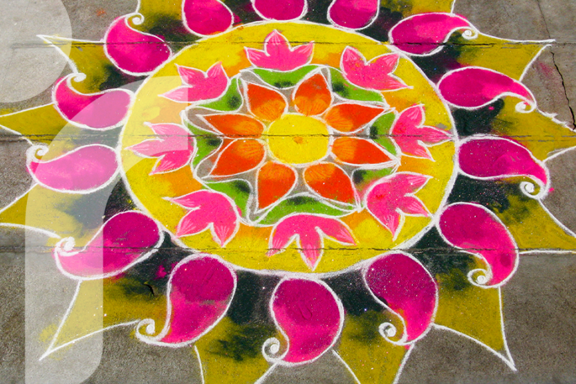 A brightly color mandala shape is on the ground created with pink, yellow, and green powders