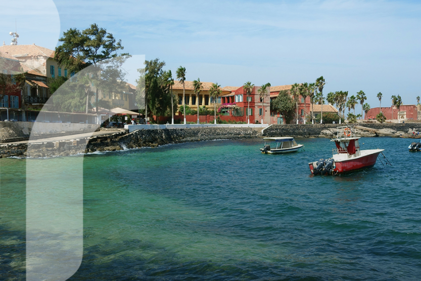 Three fishing boats are in teal water next to a colorful town with palm trees and a blue sky