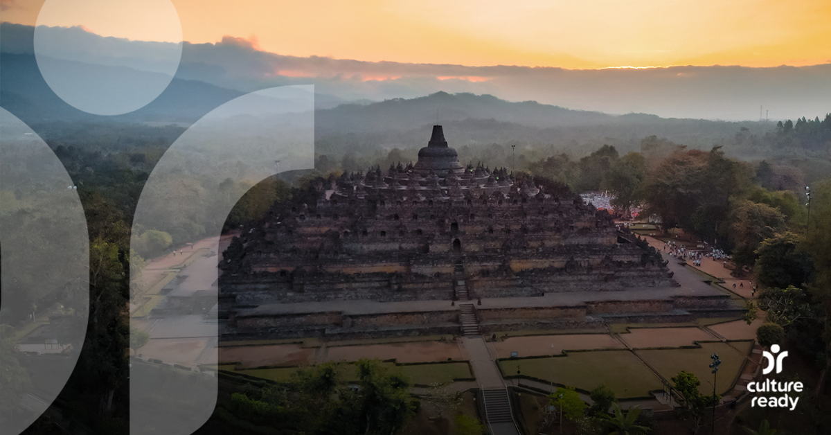 A view of the Borobudur Temple in the foreground as the sun rises over the surrounding mountains in the distance