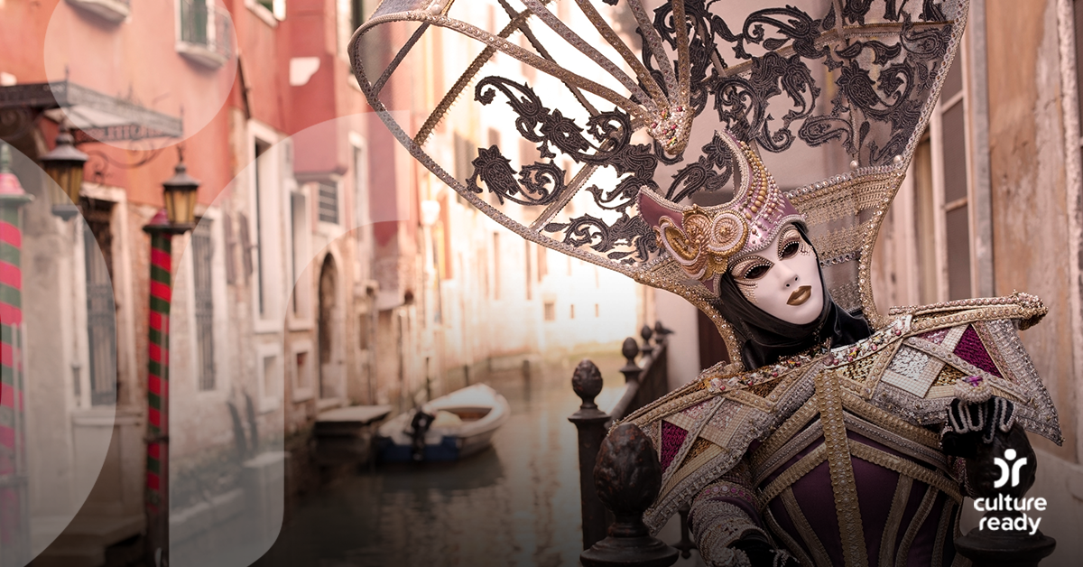 A person wearing a intricate Carnevale costume and mask floats down a canal in Venice, Italy