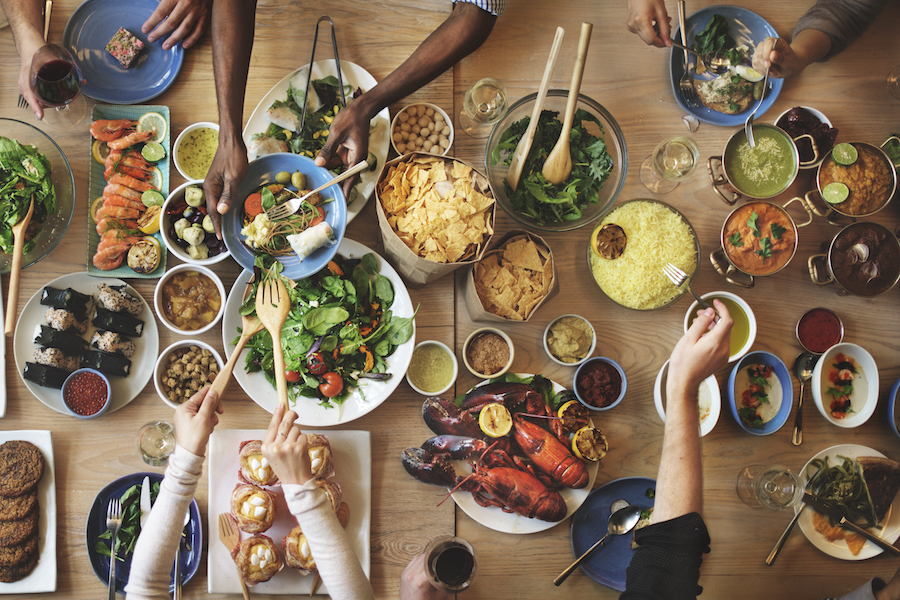 Table of many different dishes, with hands reaching in to take food
