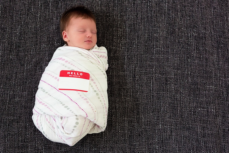 A baby swaddled in a blanket with a name tag on the blanket that says "Hello my name is."