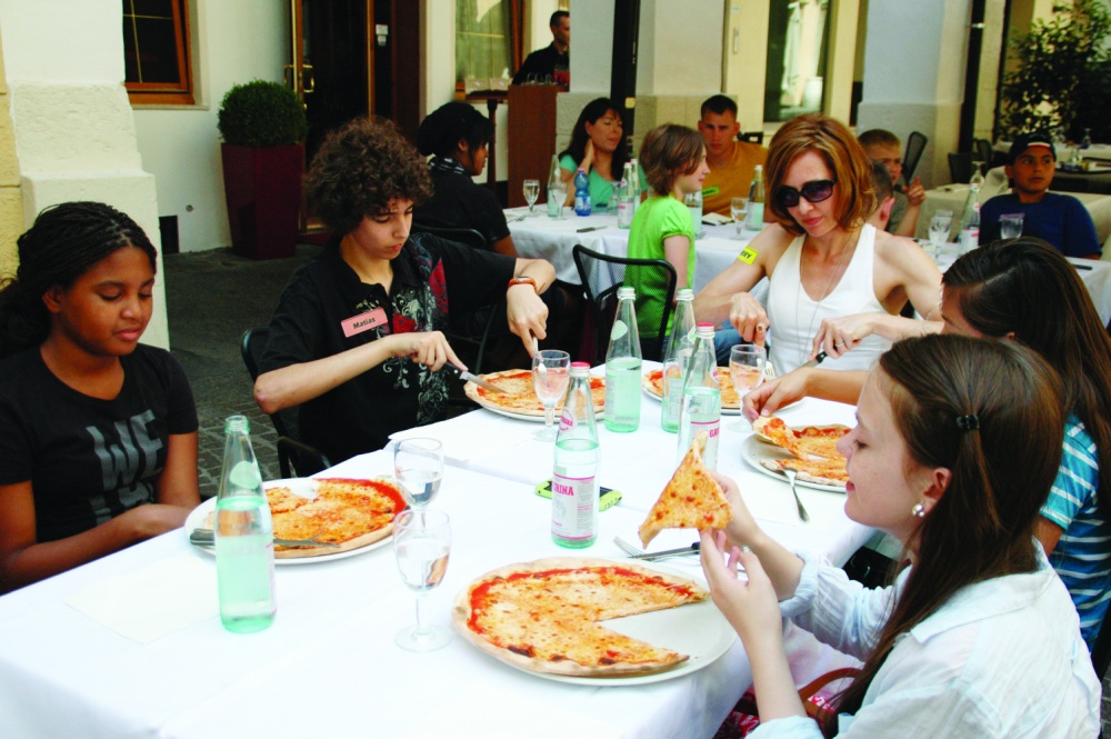 Students in the military community sit at a table eating pizza in Italy to learn cultural and regional facts.