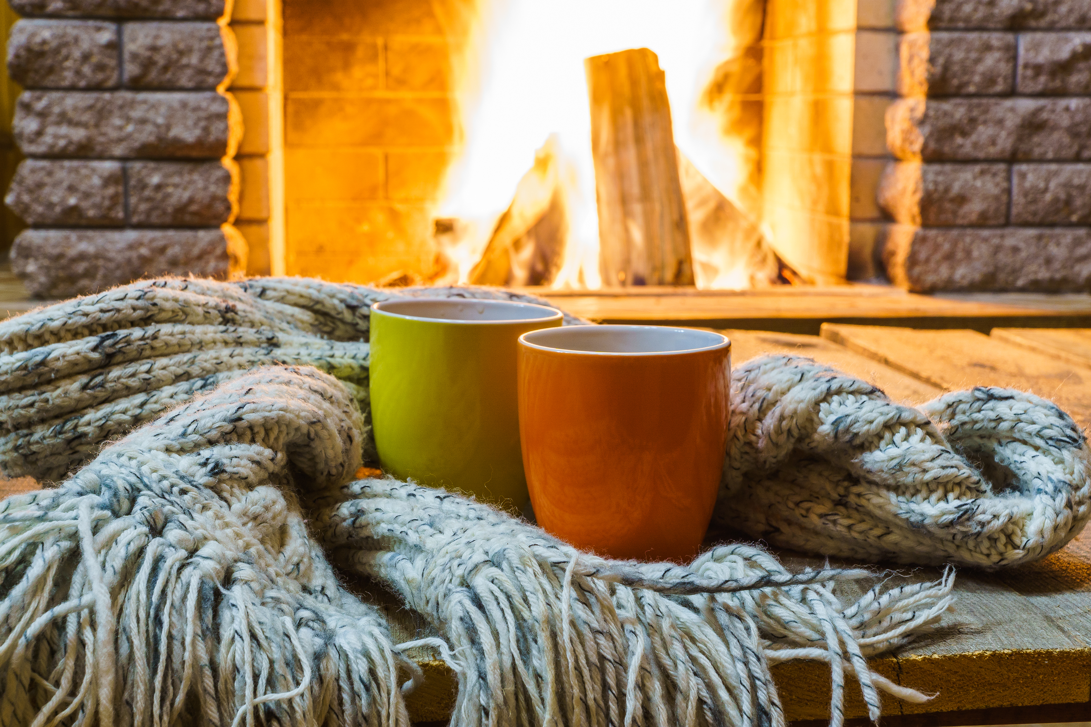 Two mugs surrounded by a blanket by a fire