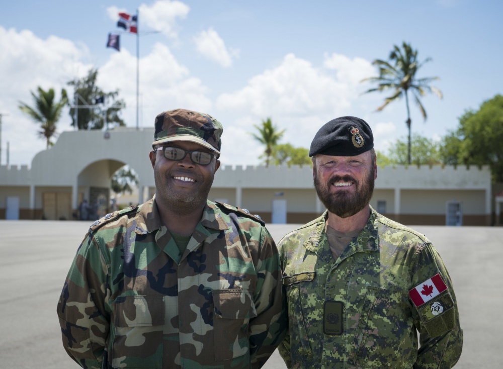 Two men in military uniforms pose for a photo outside