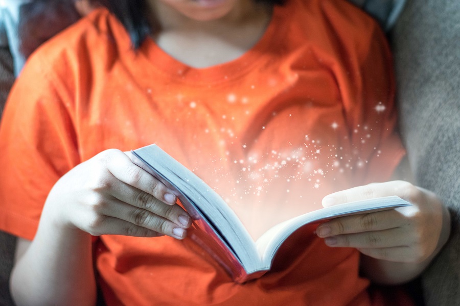 Close-up of a young girl reading a young adult fiction book with a magical sparkle light effect coming out of the book.
