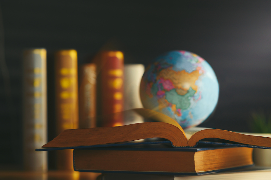 A small globe sitting on top of an open book. There are more books beneath and behind the globe.