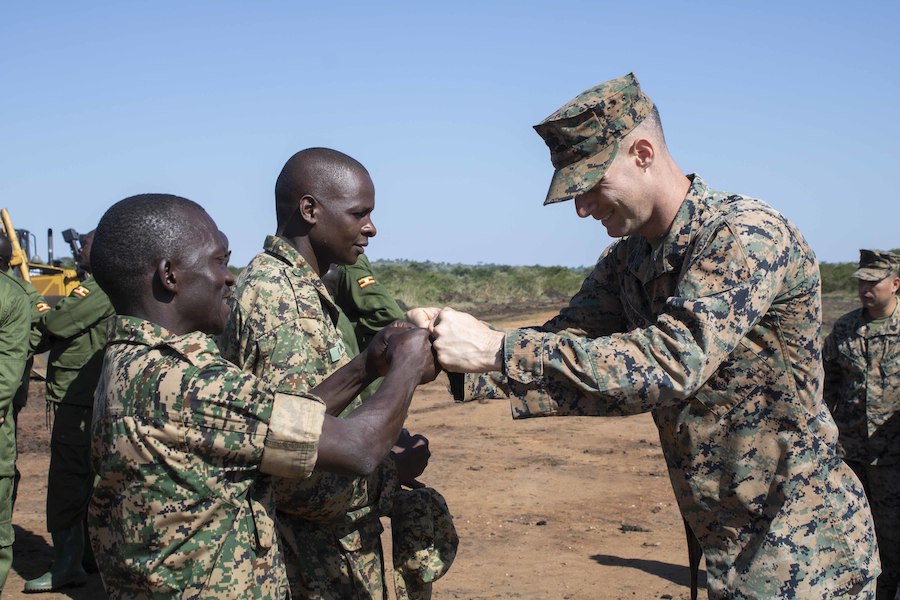 A U.S. service member greets two Ugandan service members.