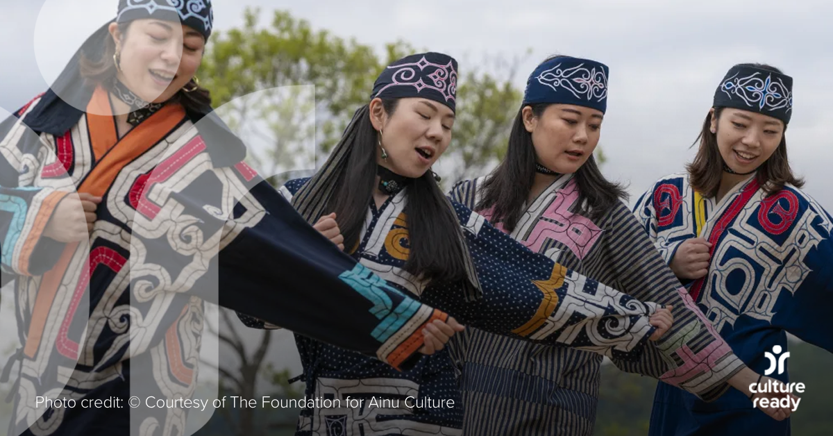 Four Ainu women in dark blue traditional clothing perform a song and dance