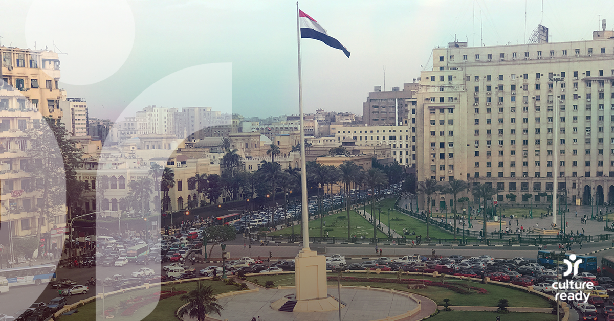 A cityscape of Cairo centers on a traffic circle with an Egyptian flag in the middle. It shows the massive traffic jam taking place on the streets of the city.