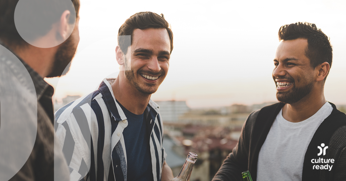 Three men in casual clothing are laughing together with a setting sun in the background 
