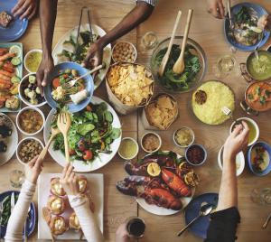 Table of many different dishes, with hands reaching in to take food