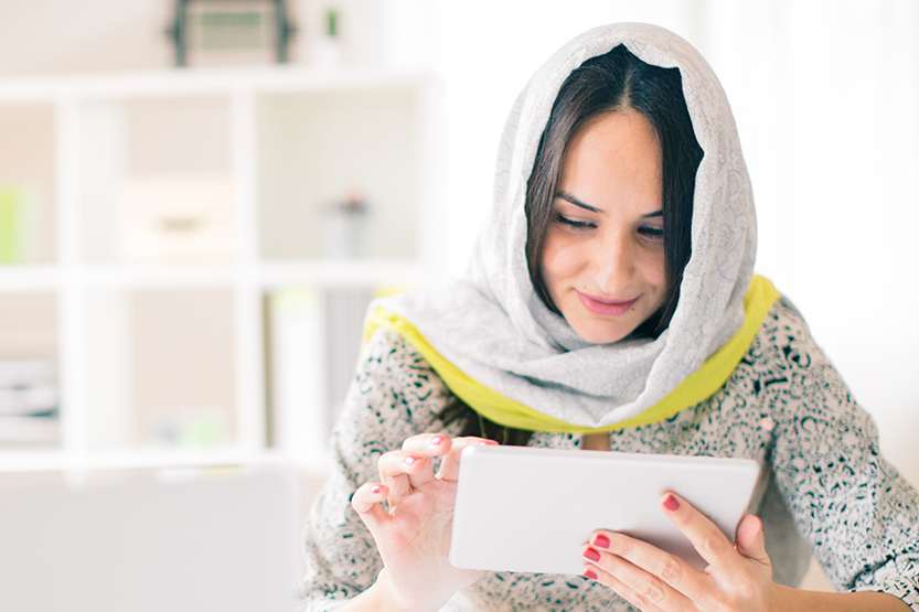 Woman wearing a scarf over her head reading an ipad