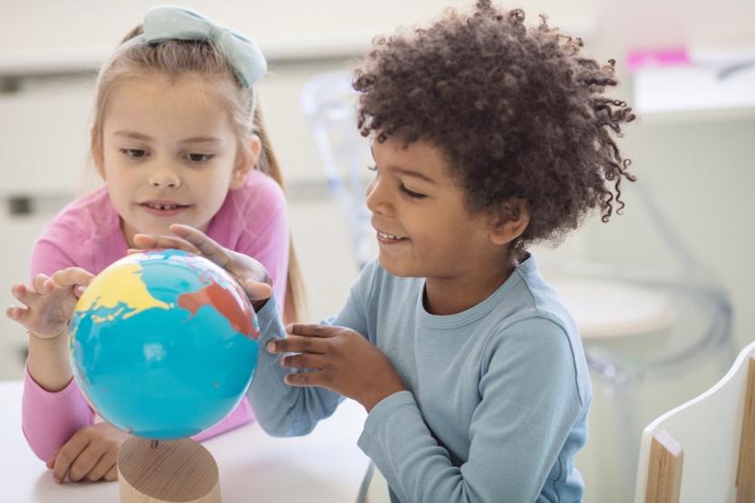 Two children sitting at a table, looking at a small globe.