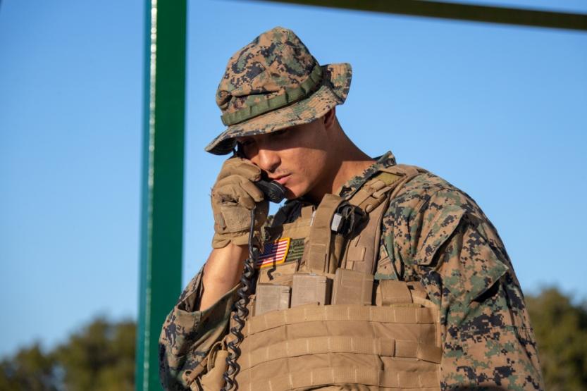 A Marine Corps radio operator is holding a phone to his hear.