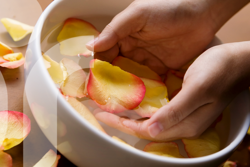 Image of two hands in a bowl of water with flower petals