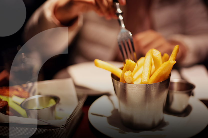 Close-up image of a cup of french fries. The person who is eating them is using a fork.