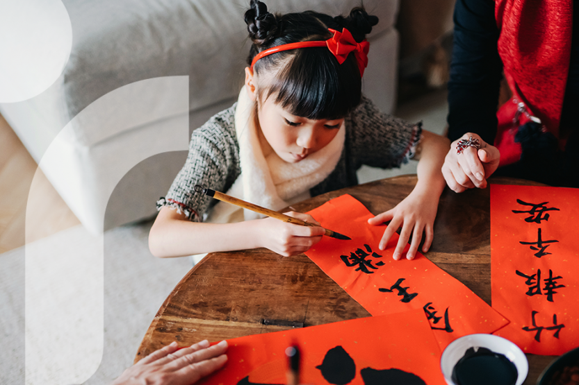 A young girl writing Chinese characters on red paper