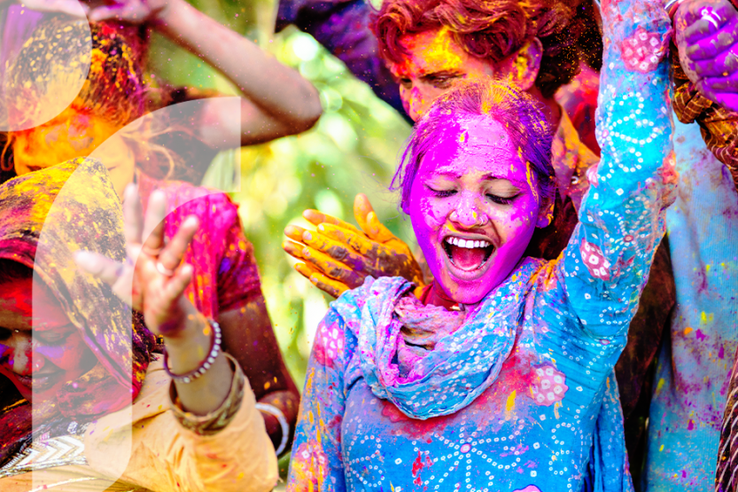 People wearing brightly colored clothing are covered in brightly colored powder as they celebrate Holi