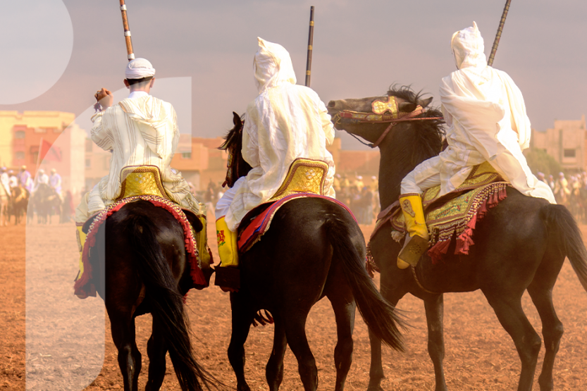 Three men dressed in white ride elaborately decorated horses participate in Tbourida