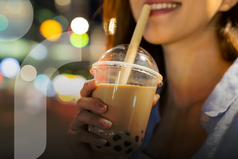 A woman drinks boba tea with lights in the background