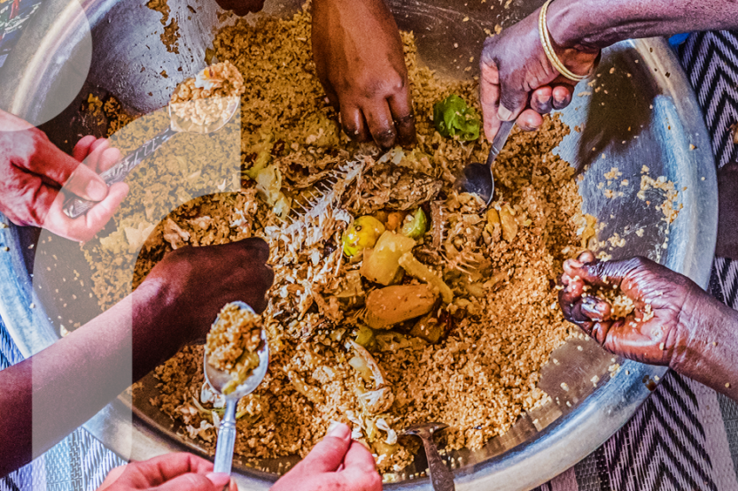 Seven hands are reaching into a communal dish of rice and fish