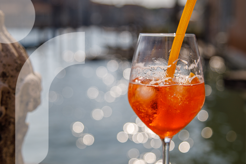 A wine glass with red wine sits in front of a sparkling river, there is a pasta straw in the glass