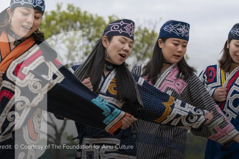 Four Ainu women in dark blue traditional clothing perform a song and dance