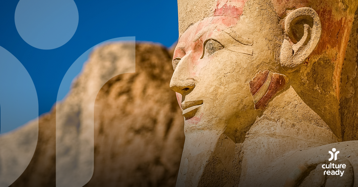 A close up image of the head of a stone statue of an ancient Egyptian female ruler in front of a blue sky
