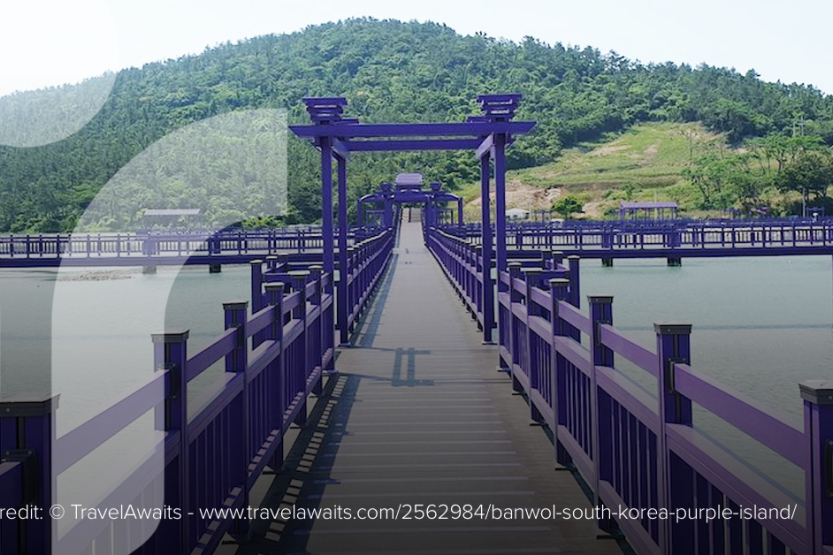 A vibrantly painted purple bridges stretches into the distance over calm water, disappearing into a green hill