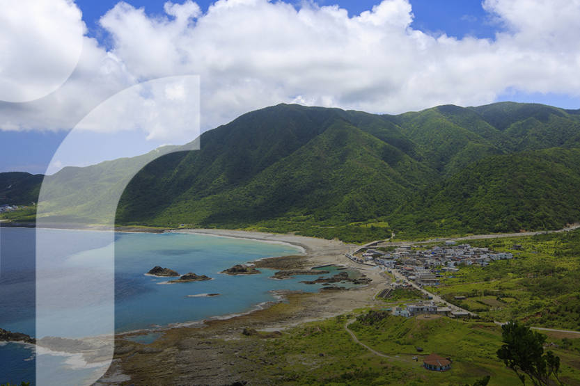 A view of Orchid Island showing green hills, a bright blue bay, the Tao city and blue sky
