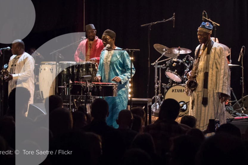 Five members of Orchestra Baobab wearing traditional Senegalese clothing play instruments on stage