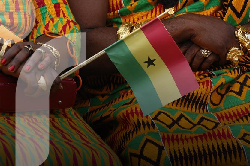 Two women in colorful clothing and jewelry hold a small Ghana flag.