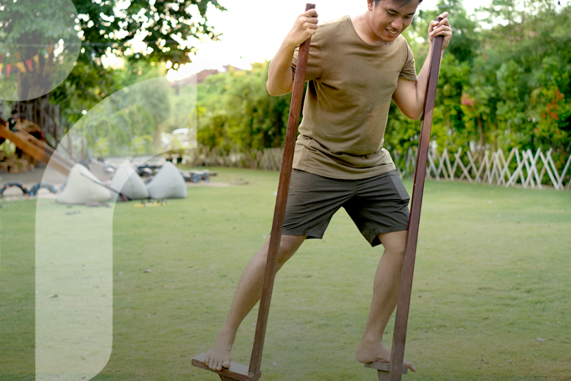 A man wearing green shorts and a green t-shirt practices using bamboo stilts in a field
